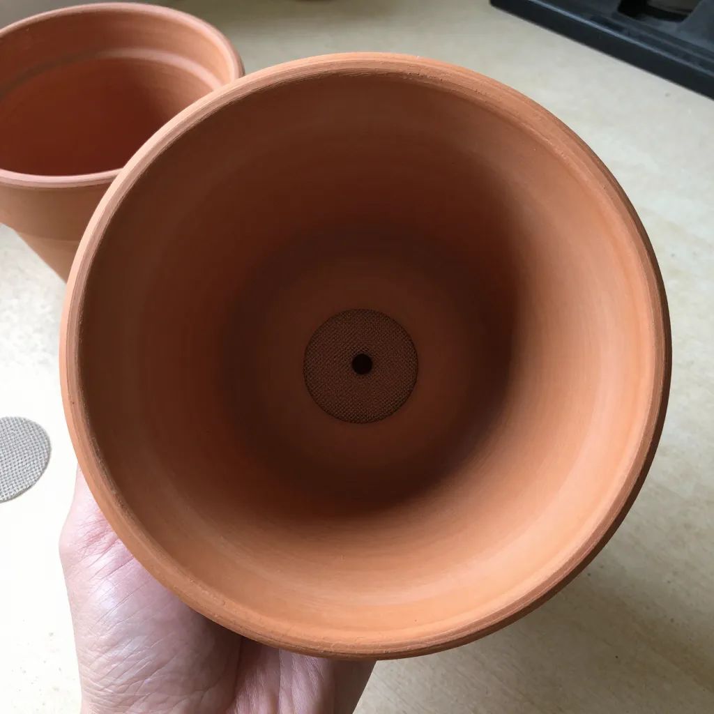 Fundo de vaso de barro com tela cobrindo o furo de drenagem
