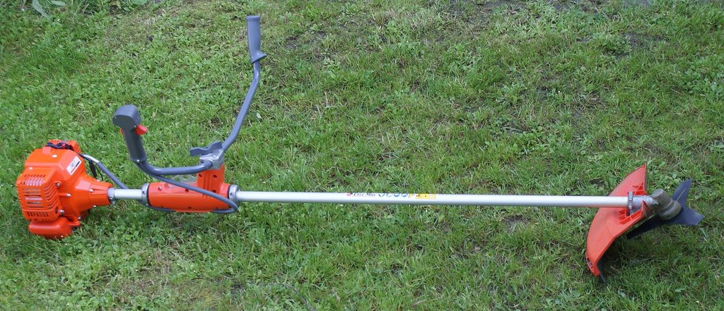 Roçadeira lateral apoiada sobre gramado, com lâmina de corte na ponta